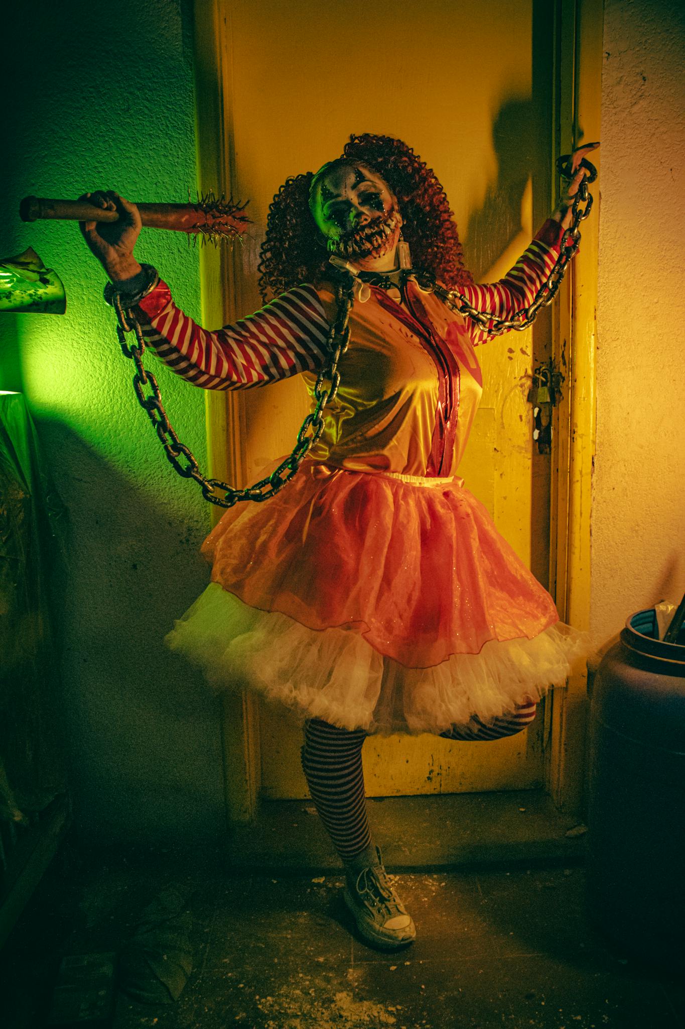 A terrifying clown character in full costume, posing menacingly with chains and dramatic lighting.