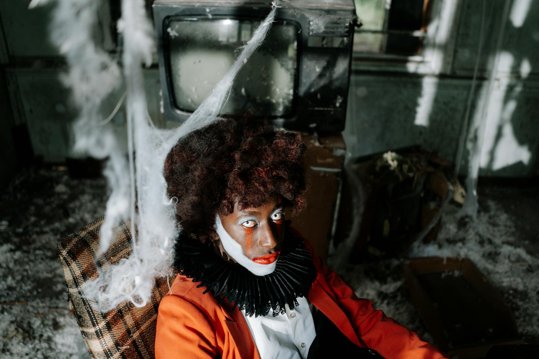 Creepy clown in an abandoned room filled with cobwebs, creating a spooky Halloween ambiance.