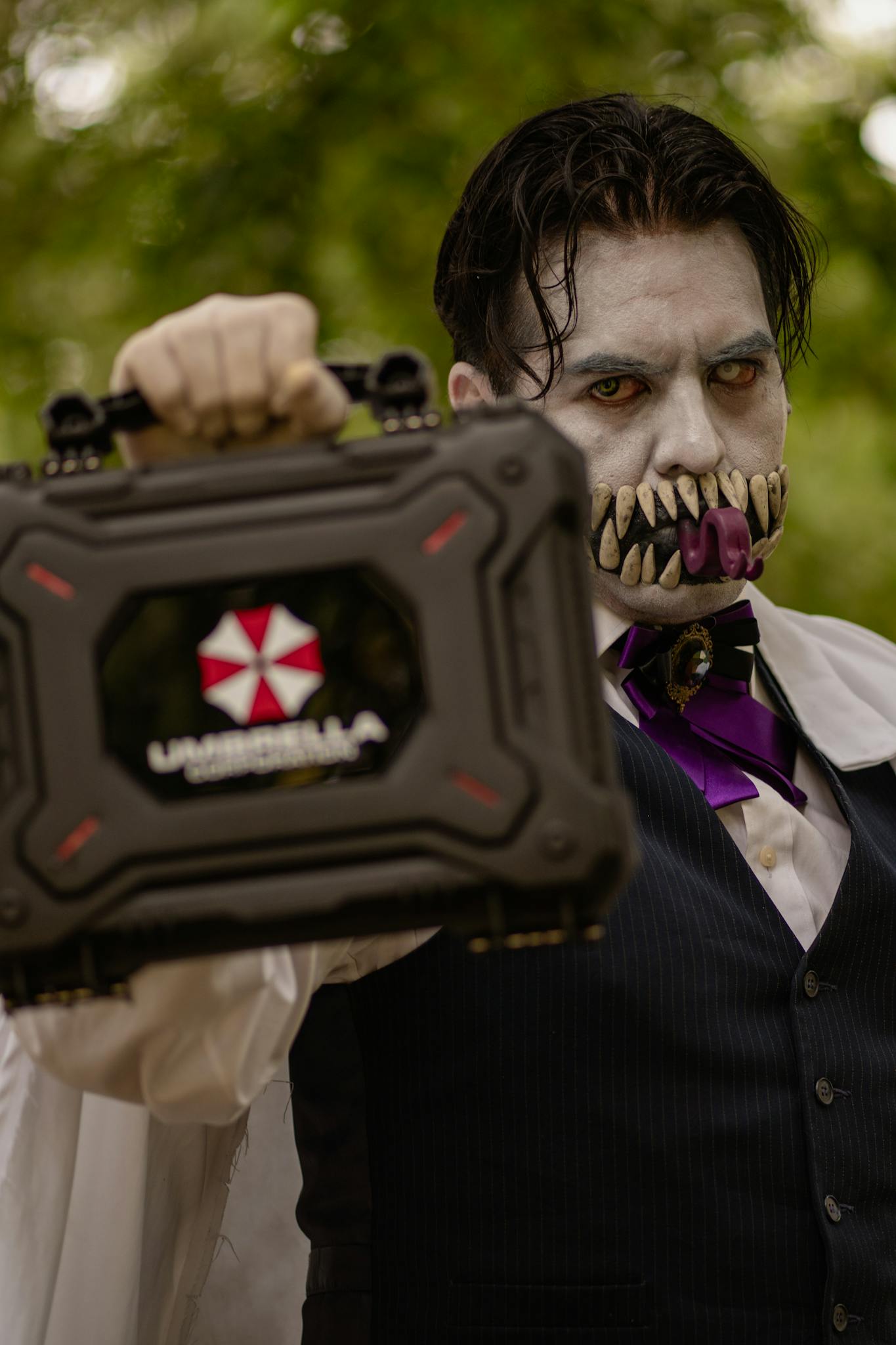 Gruesome cosplayer dressed as a character, holding a branded case in an outdoor setting.